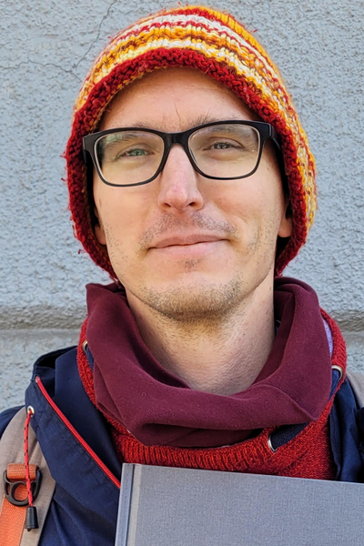 The middle-aged male speaker wearing a colourful hat and glasses