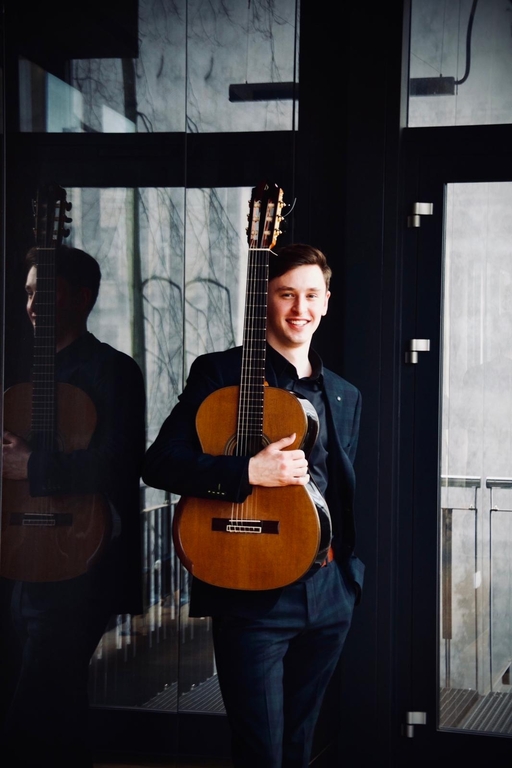 Maksym Niewczas wearing a dark suit and holding a guitar