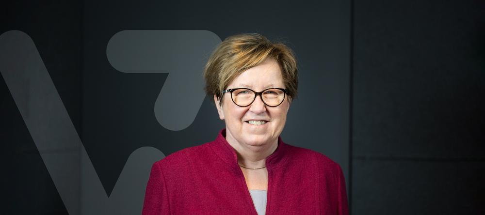 Prof. Bryszewska on a dark background, next to a V-shaped graphic