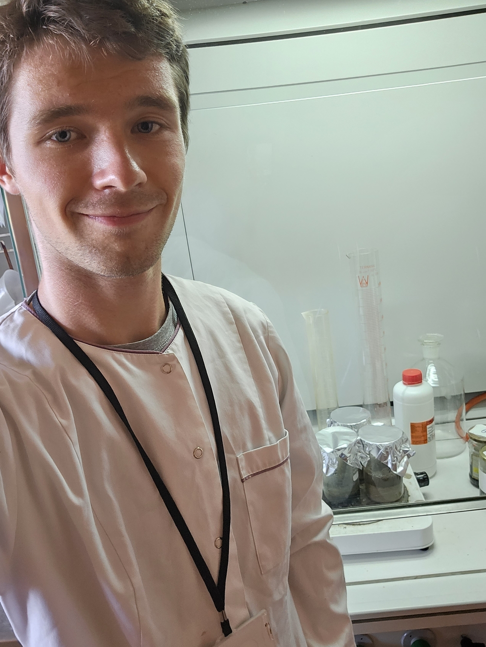 Jarosław Brodecki wearing a white protective coat and standing in the laboratory where he conducts his research